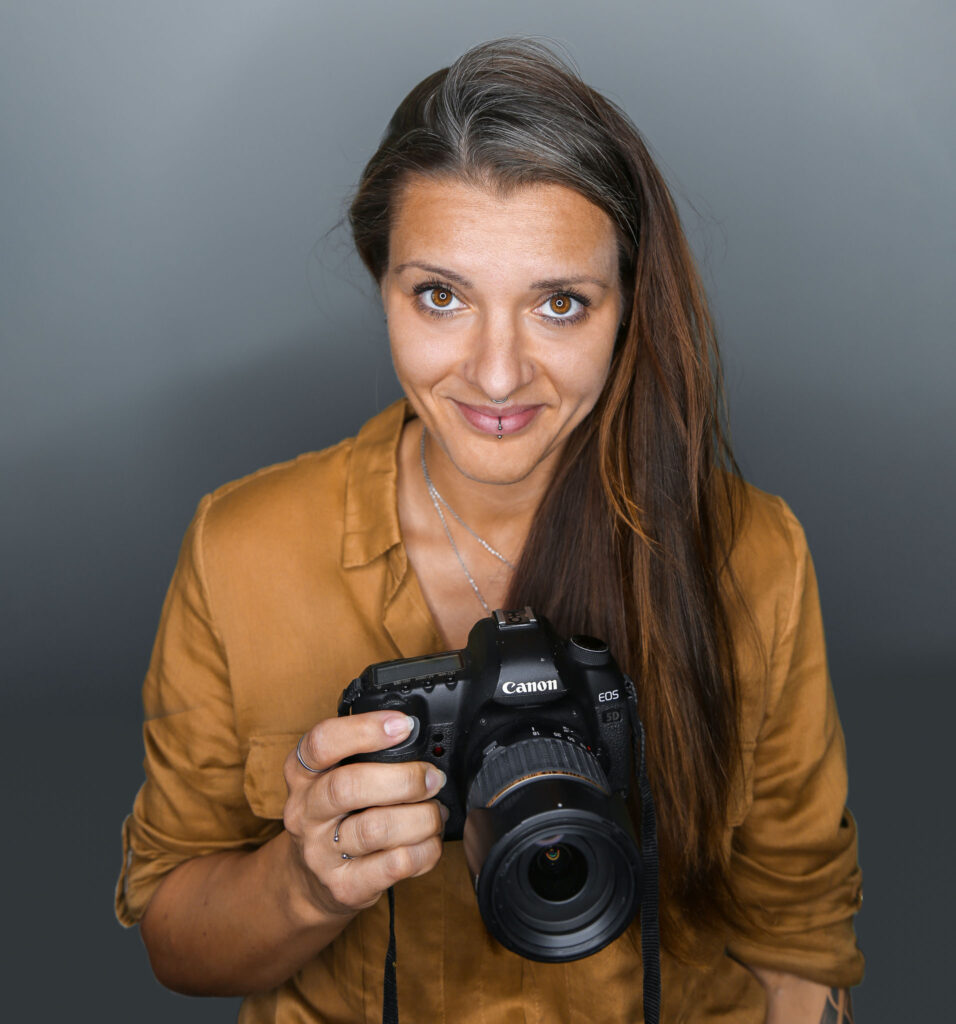 Selbstportrait einer Fotografin auf Rügen, Fotograf Rügen, und Umgebung mit Kamera und herausforderndem Lächeln