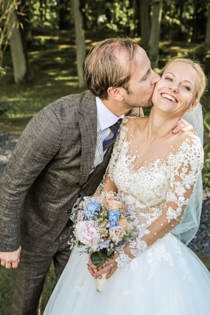 Romantischer Kuss: Der Bräutigam küsst die strahlende Braut, ihr atemberaubendes Kleid und der prächtige Brautstrauß im Fokus. #Fotografin auf Rügen