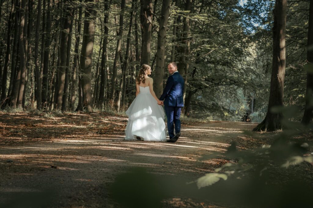 Das Brautpaar läuft Hand in Hand durch den Nationalpark Jasmund auf Rügen. Er dreht sich um und schaut in die Kamera, während sie ihn verliebt anschaut.